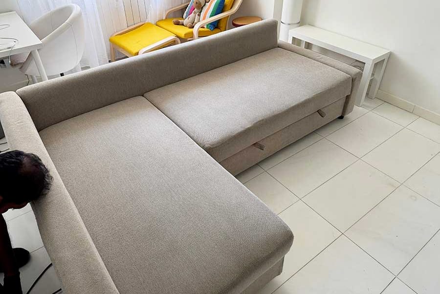 Un divano letto estraibile beige si estende in un soggiorno luminoso e moderno con pavimenti piastrellati bianchi, perfetto per chi cerca il lavaggio divano domicilio zona Affori Milano.