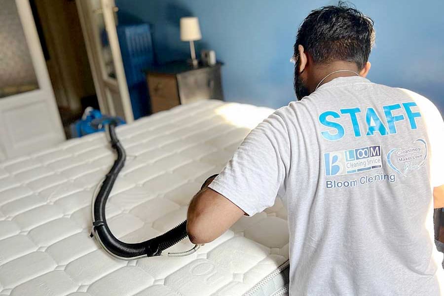 Un membro del personale esegue il lavaggio materasso a domicilio Milano, pulendo un materasso con un tubo di aspirazione in una camera da letto ben illuminata.
