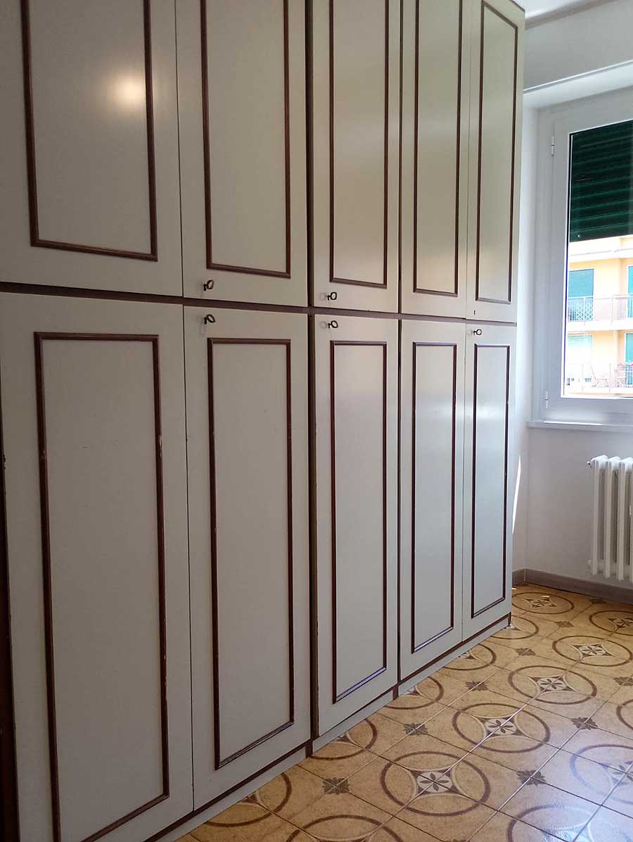 Armadietti alti color crema con rifiniture marroni accanto a una finestra, sopra un pavimento di piastrelle a motivi: perfettamente rinnovati dopo lo sgombero e la pulizia post imbiancatura Milano.