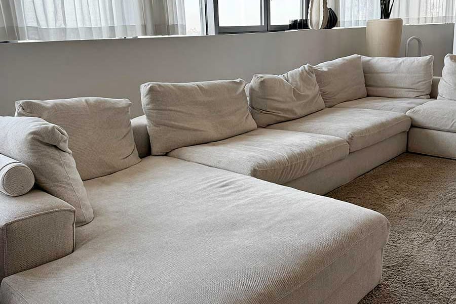 Un grande divano componibile beige con cuscini morbidi in un soggiorno moderno con luce naturale soffusa, perfetto per lavare il divano tessuto chiaro Milano e mantenere il vostro spazio fresco e invitante.
