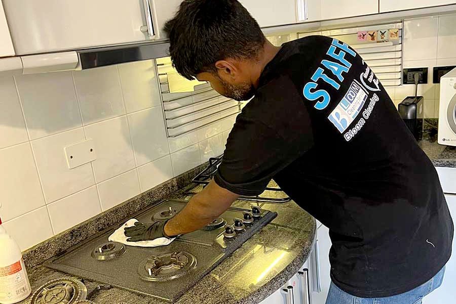 Persona con guanti che pulisce un piano cottura in una cucina moderna, con materiale di pulizia nelle vicinanze - perfetto per chi cerca servizi di pulizia appartamento zona Turati Milano.