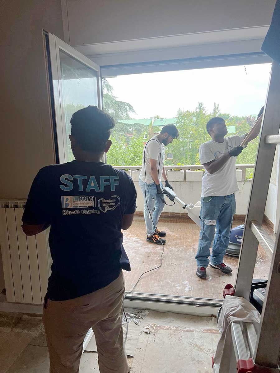 Tre uomini puliscono un balcone in Zona Moscova, Milano; uno indossa una maglietta "STAFF" e si trova all'interno vicino a una porta a vetri aperta, specializzata in pulizia appartamenti.