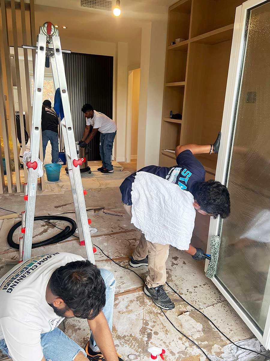 Quattro operai ristrutturano una stanza in Zona Moscova, a Milano, dipingendo e pulendo con attrezzi, scala e materiali sparsi sul pavimento-Pulizia Appartamenti in corso.