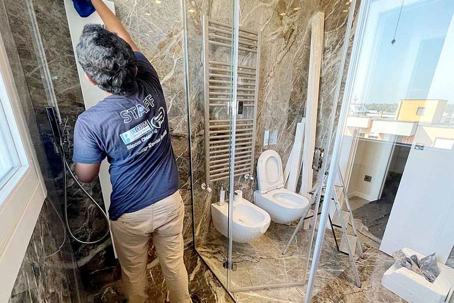 Una persona sta pulendo un bagno moderno con doccia in vetro, wc, bidet e pareti e pavimento in marmo in un elegante appartamento di Milano in Zona Moscova, vetrina di Pulizia Appartamenti.