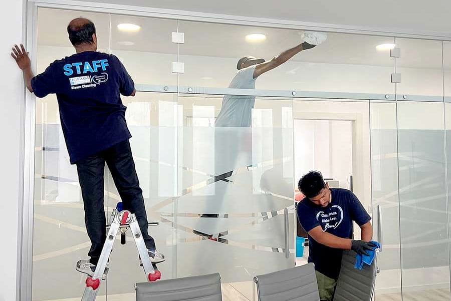 Tre operai eseguono la pulizia uffici zona Missori: uno su una scala, uno che pulisce la parete di vetro dell'ufficio, e un altro concentrato sull'igienizzazione sedie ufficio Milano.