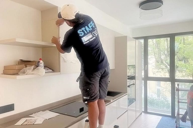 Un operaio in pantaloncini corti sta installando un mobile in una cucina moderna e luminosa con grandi finestre durante un cambio di inquilino in un appartamento vicino a P.za Napoli.
